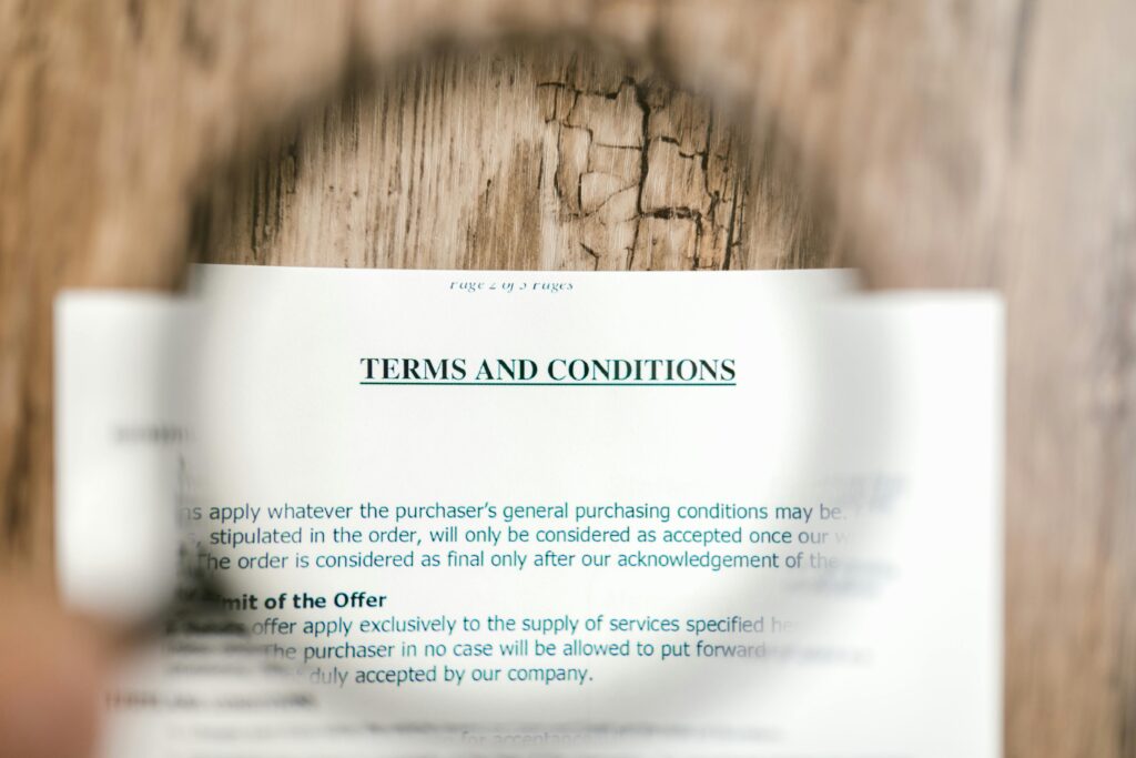 Magnifying glass focusing on terms and conditions document on wooden surface.