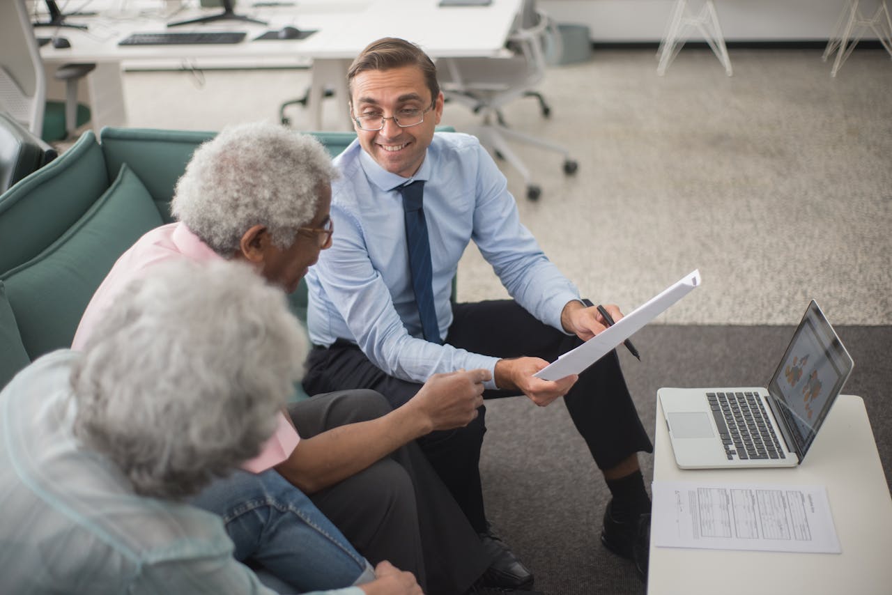 Consultant discussing financial plans with senior clients in a modern office setting, using documents and a laptop.